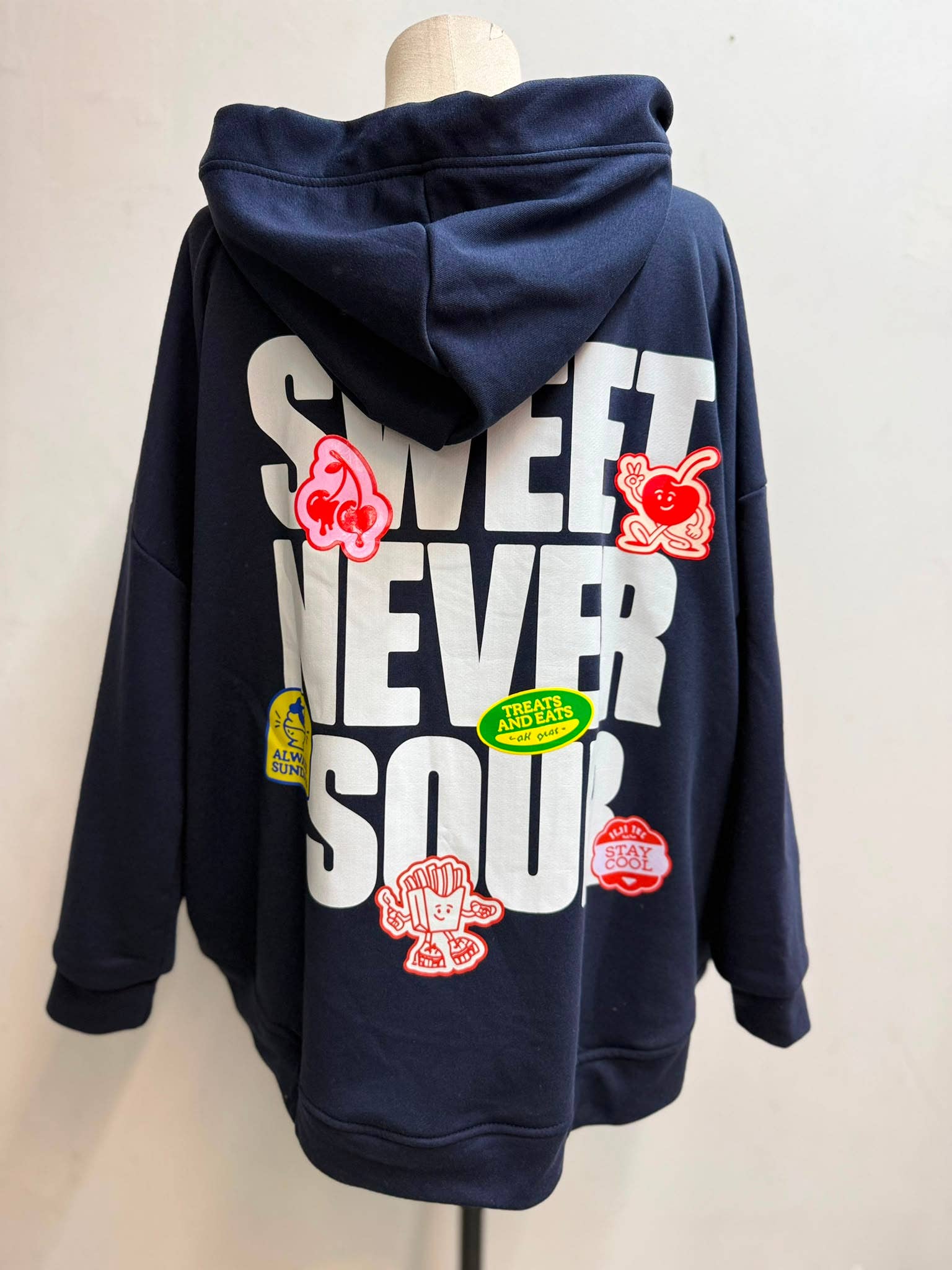 Oversize Hoodie Sweet Never Sour in Marineblau – Rückenansicht auf Schneiderpuppe mit großem Print und bunten Cartoon-Patches