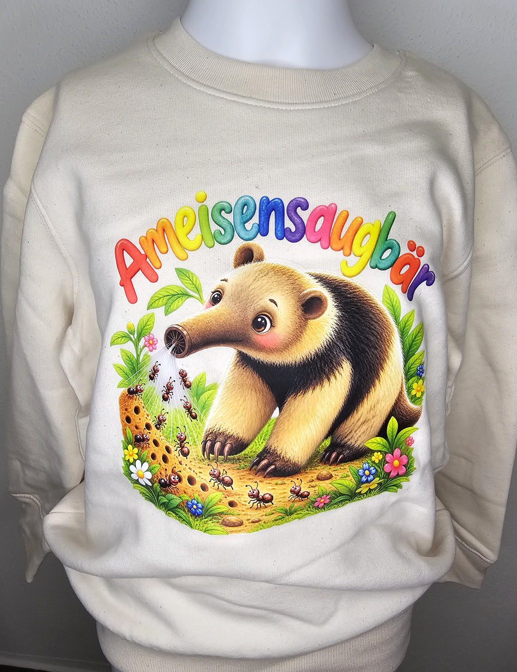 Kinder-Sweatshirt Ameisensaugbär aus Bio-Baumwolle in Naturweiß mit buntem Ameisenbär-Motiv und Regenbogenschrift, Vorderansicht auf Schneiderpuppe